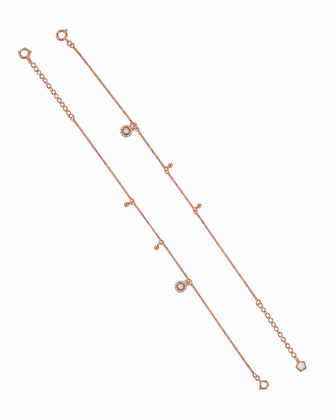 A delicate rose gold anklet with multiple small dangling bead links and two round bezel-set clear stones, displayed diagonally on a solid white background.