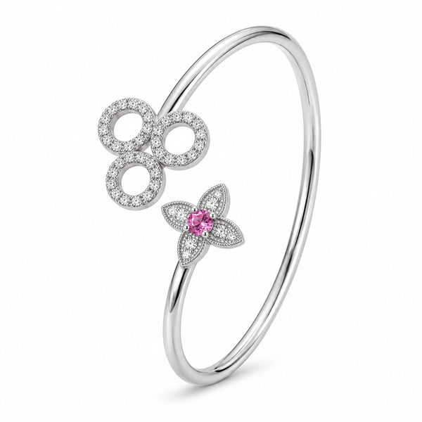 A polished silver-tone open bangle bracelet featuring a large circular floral motif paved with small clear stones and a smaller four-petal flower with a central pink gemstone, shown on a white background.
