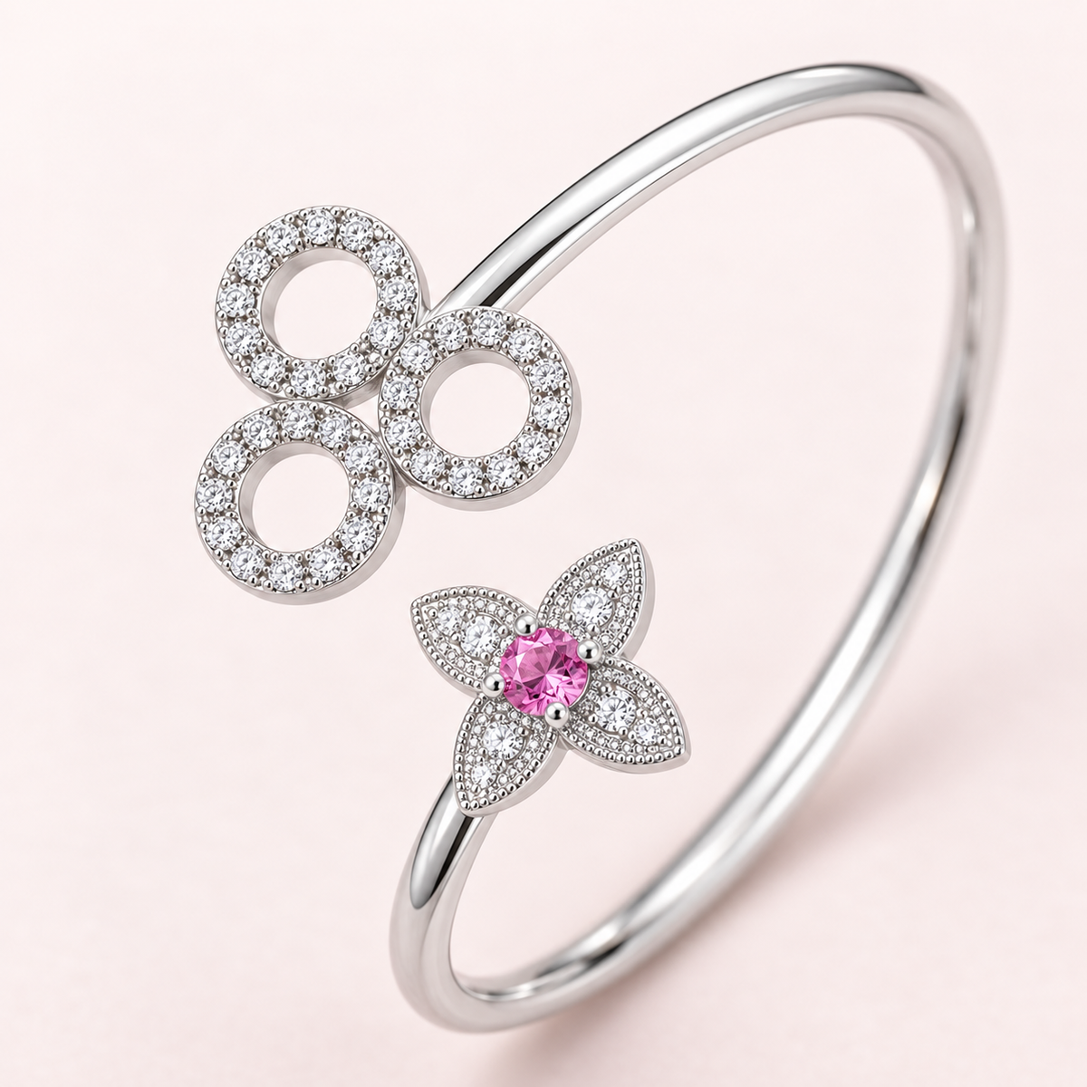 A silver-toned hinged bangle bracelet featuring a flower motif with a central pink gemstone and three circular openwork motifs paved with clear stones, set against a soft pink background.