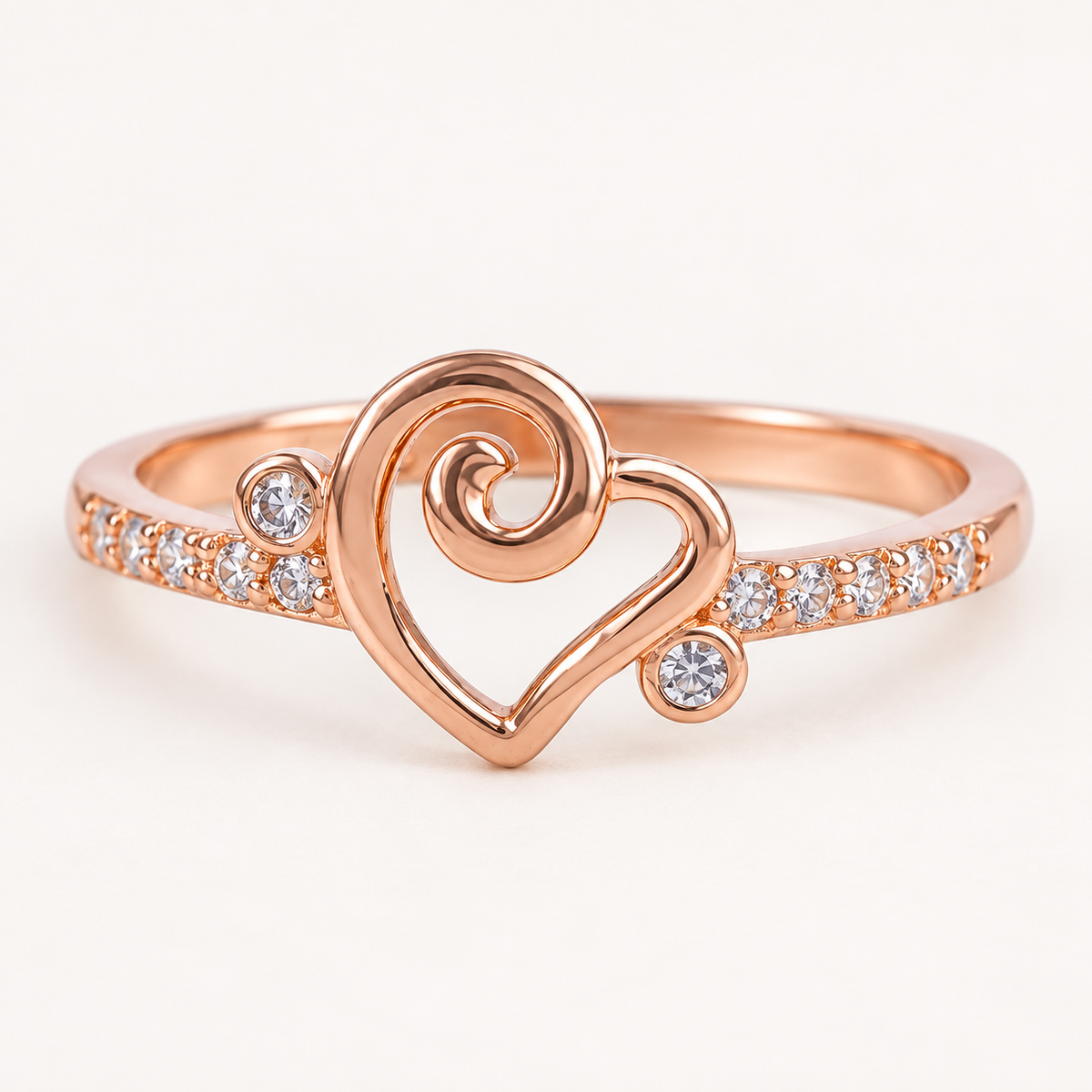 Angled view of Amora Swirl Heart rose gold-tone ring with a slim stone-studded band