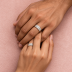 Couple wearing matching silver rings with two rows of sparkling stones on a soft blush-pink background.