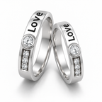 Two silver wedding bands with the word 'Love' engraved on the outer surface, each featuring a round clear stone and a small row of three clear stones, set against a clean white background.