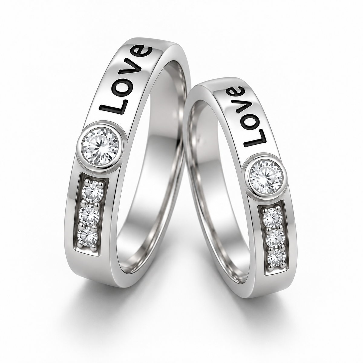 Two silver wedding bands with the word 'Love' engraved on the outer surface, each featuring a round clear stone and a small row of three clear stones, set against a clean white background.
