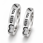 Two matching silver-toned rings engraved with 'KISS YOU' and decorated with black heart outlines and clear rhinestones, shown on a white background.