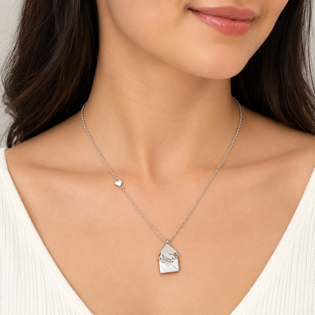 A close-up of a woman wearing a delicate silver chain necklace with a small engraved house-shaped pendant and a tiny heart accent.