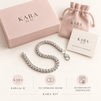 A silver chain bracelet with a lobster clasp is displayed on a cream background with its branded packaging, including a pink box, a pink drawstring pouch, an authenticity certificate, and three circular product callouts at the bottom. The brand name 'KARA by SJ' is clearly visible.