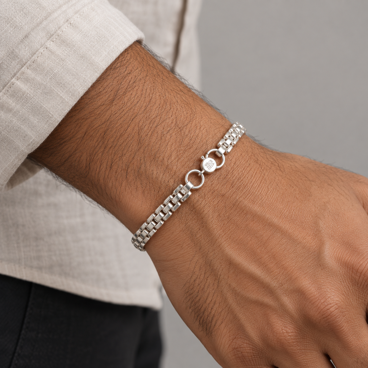 A silver-toned metal bracelet with a textured link chain, two interlocking circular rings, and a small round charm, shown worn on a person's wrist.