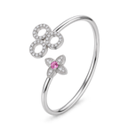 A silver-toned open bangle bracelet featuring a large circular motif paved with clear stones and a smaller flower motif with a central pink gemstone, shown on a white background.