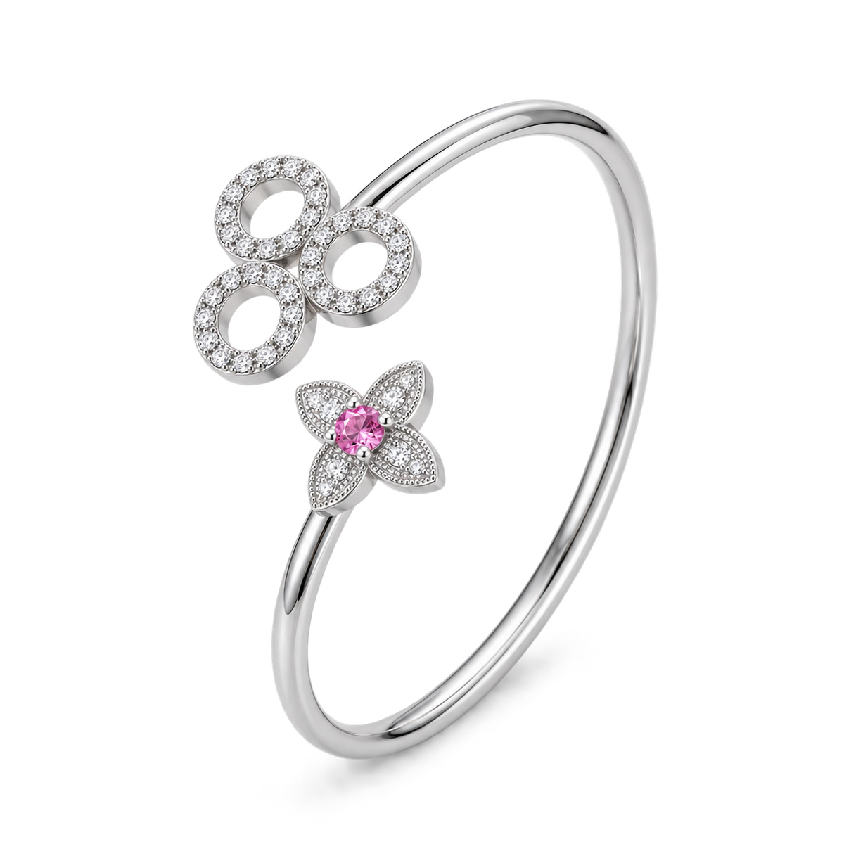 A silver-toned open bangle bracelet featuring a large circular motif paved with clear stones and a smaller flower motif with a central pink gemstone, shown on a white background.