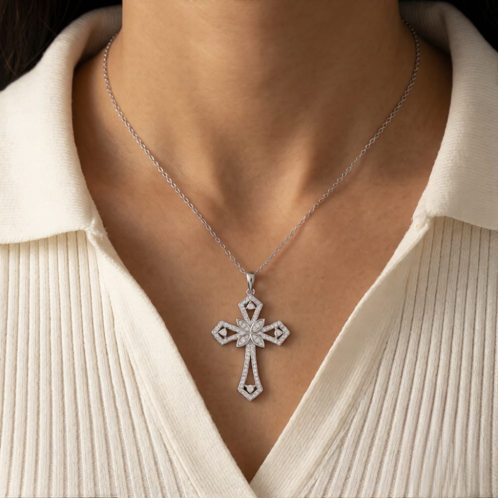 A silver cross pendant necklace with sparkling clear stones, worn on a model's neck over a cream-colored ribbed top.